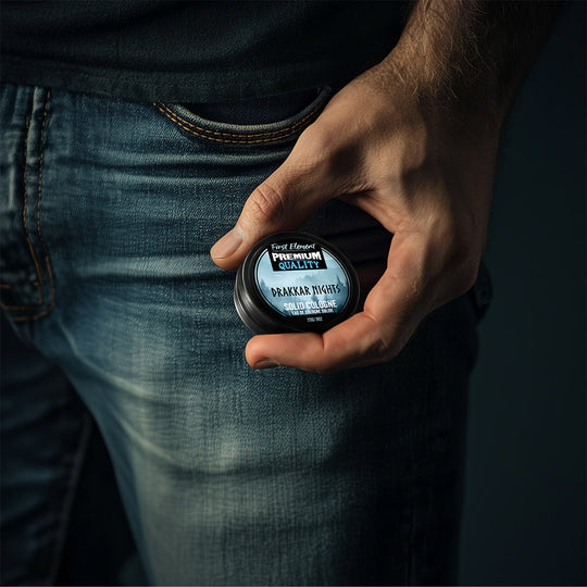 Hand holding a small solid cologne in front of his jeans pocket. Showing the size is pocket sized and easy to travel. 