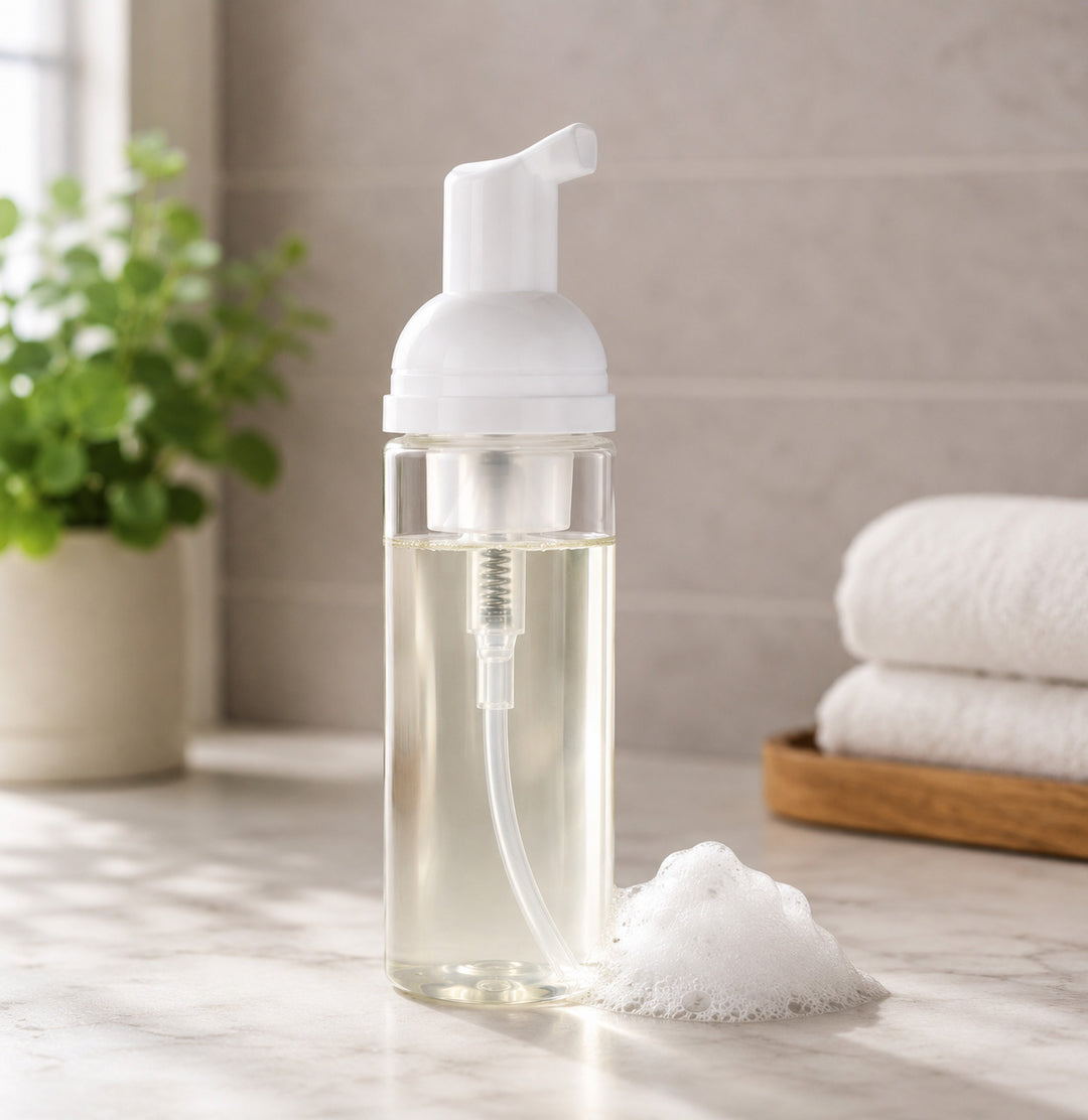 Foam soap dispenser with a white pump on a bathroom counter, next to folded towels and a plant.