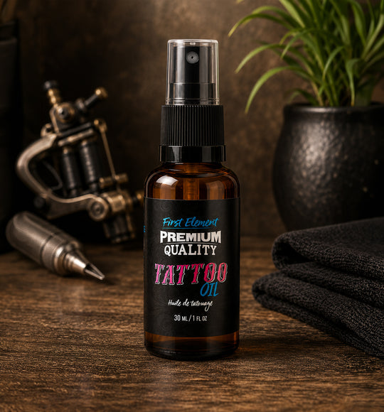 Bottle of tattoo oil with a black label on a wooden surface, surrounded by tattoo equipment.
